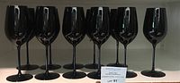 Row of 11 black stemmed wine glasses on shelf with auction lot card