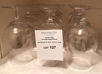 Set of 12 clear crystal beer glasses with stems, arranged in rows upside down showing their bases, with a card labeled LOT 127 in front.