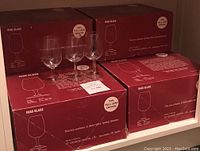 Four boxed sets of INA0 wine tasting glasses and three individual crystal glasses displayed in front of the boxes.