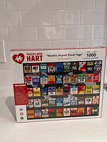 Box of Puzzles With Hart 1000 piece jigsaw puzzle showing the airport travel tag design, front of box.