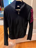 Front view of the black Bench funnel neck sweater hanging, showing full zip and pink Bench logo on sleeve