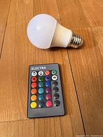 Photo of Electra smart LED light bulb and the remote control on wooden floor.