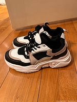 Side view of women's black, white, beige and brown fashion sneakers with chunky white platform sole on wooden floor.