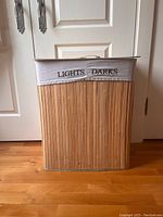 Front view of a bamboo laundry basket featuring a white fabric band labeled for sorting lights and darks laundry.