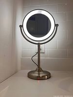 Front view of the round cosmetic mirror with illuminated LED ring light on metal stand showing light on.