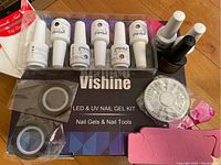 Photo of Vishine LED & UV Gel Kit including 5 bottles of gel nail colors, base coat, top coat, sealer, nail tool wheel with gems, and nail tip guides in packaging.