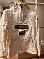 Front view of white Napapijri women's jacket hanging on door with visible front pocket and hood.