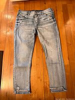 Front view of light blue Silver Jeans Suki Mid Straight style jeans showing faded wash, distressing and frayed hems on wooden floor.