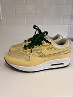 Side view of one Nike Air Max Lemonades shoe in light yellow with dark green laces on white sole.