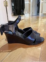 Side view showing black leather wedge heel sandal design with ankle strap and buckle.