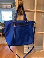 Front view of large royal blue Huser tote bag with dual handles and detachable strap, hanging on door handle.