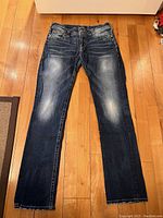 Front view of dark blue jeans with light fading on thighs and knees, straight leg style laid flat on floor.