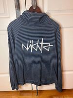 Rear view of blue and black striped hoodie with Nikita logo on back, hanging on wooden hanger