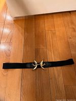 Black elastic and leather women's belt laid flat on wooden floor