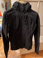 Front view of black Lululemon scuba sweater on hanger showing full zip and high collar, with subtle textured pattern.