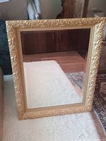 Full view of rectangular antiqued mirror with bevelled glass and ornate gold frame standing on floor.
