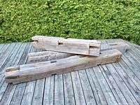 Three weathered antique hardwood barn beams stacked on a wooden deck showing joints and natural aging.