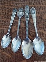 Four silver commemorative spoons laid out on wooden surface showing full length and front design.