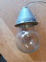 Full side view of the explosion proof light fixture showing the glass globe and metal conical top with wire attached.