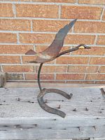 Front-left angled view of the metal Canada goose sculpture mounted on a horseshoe base against a brick wall background.