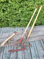 Hatchet and two brush cutters placed on a wooden beam on a deck with greenery in the background