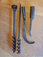 Four hand forged manual tools including two spiral augers and two barn construction tools displayed on wooden surface