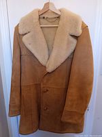 Front view of tan lambskin leather coat with shearling collar and button closure on hanger.