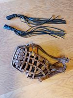 The leather dog training muzzle lying flat showing the basket weave design of the straps and buckles.