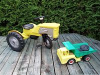 Pedal tractor and dump truck shown on wooden deck with greenery background showing full lot items.