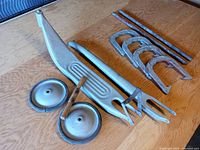 Photo showing all metal parts including scooter platform, wheels with wooden handles, front fork, horseshoes, and rods laid out on table.