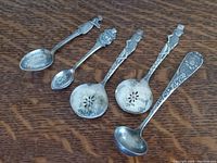 Five vintage advertising silver spoons arranged on wood surface showing various designs and tarnish.