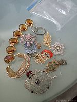 Group of assorted vintage rhinestone jewelry pieces including bracelets, brooches, and pendants displayed on a flat surface, showing variety in size and colors.