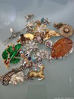 Top-down image showing the vintage rhinestone jewelry group including various brooches with rhinestones and colored enamel, clip earrings, a faux amber pendant, and faux pearl details.
