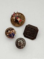 Front view of four vintage service club lapel pins showing different designs including Red Cross, 4-H, Knight's of Columbus, and another figure.