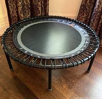Front view of entire Bellicon mini rebounder trampoline on wood floor with patterned curtains in background.