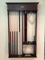 Full front view of wall-mounted cue rack holding cues, triangle racks, chalk and brush