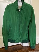 Front view of kelly green nylon bomber jacket hanging on door