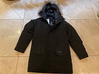 Full front view of black parka laid flat on floor