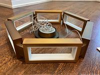 Hexagonal arrangement of six bronze rectangular frames with white diffusers around central canopy and bundled suspension wires on wood floor