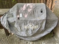 Protective Napoleon-branded fabric cover draped over grill, shows overall coverage and logo