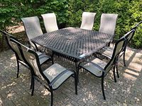Wide view of square metal patio table and eight sling chairs set on brick patio