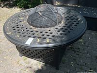 Front view of round metal fire pit table with lattice base and mesh dome cover