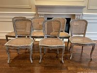 Six French style caned chairs with distressed painted frames arranged in two rows on hardwood floor