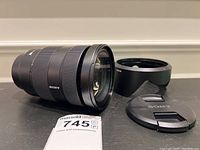 Lens body on its side with hood and front cap beside it