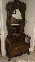 Full view of carved oak hall seat with oval mirror, arm rests and storage bench.