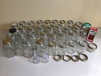 38 glass canning jars arranged on white surface with lids and rings, displaying variety of sizes and shapes.