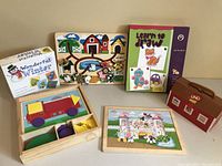 Lot of children's educational toys including puzzles, drawing book, card games arranged on a table under neutral lighting.