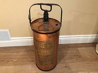 Front angle view of copper fire extinguisher with pump handle and embossed brass label showing brand and usage instructions.