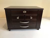 Front view of the dark wood jewelry box displaying four drawers with silver handles and a lock on the top drawer.