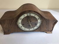 Front view showing the wooden curved body of the mantle clock and glass-covered clock face